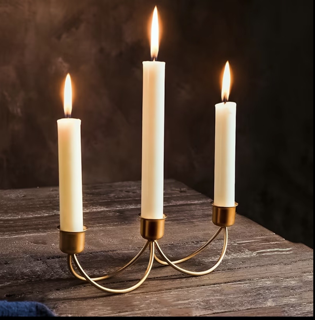 Low brass swan-neck candelabra holding three lit taper candles