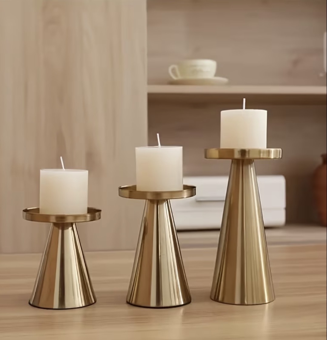 Three brass candelabras with curly scroll arms and lit pillar candles