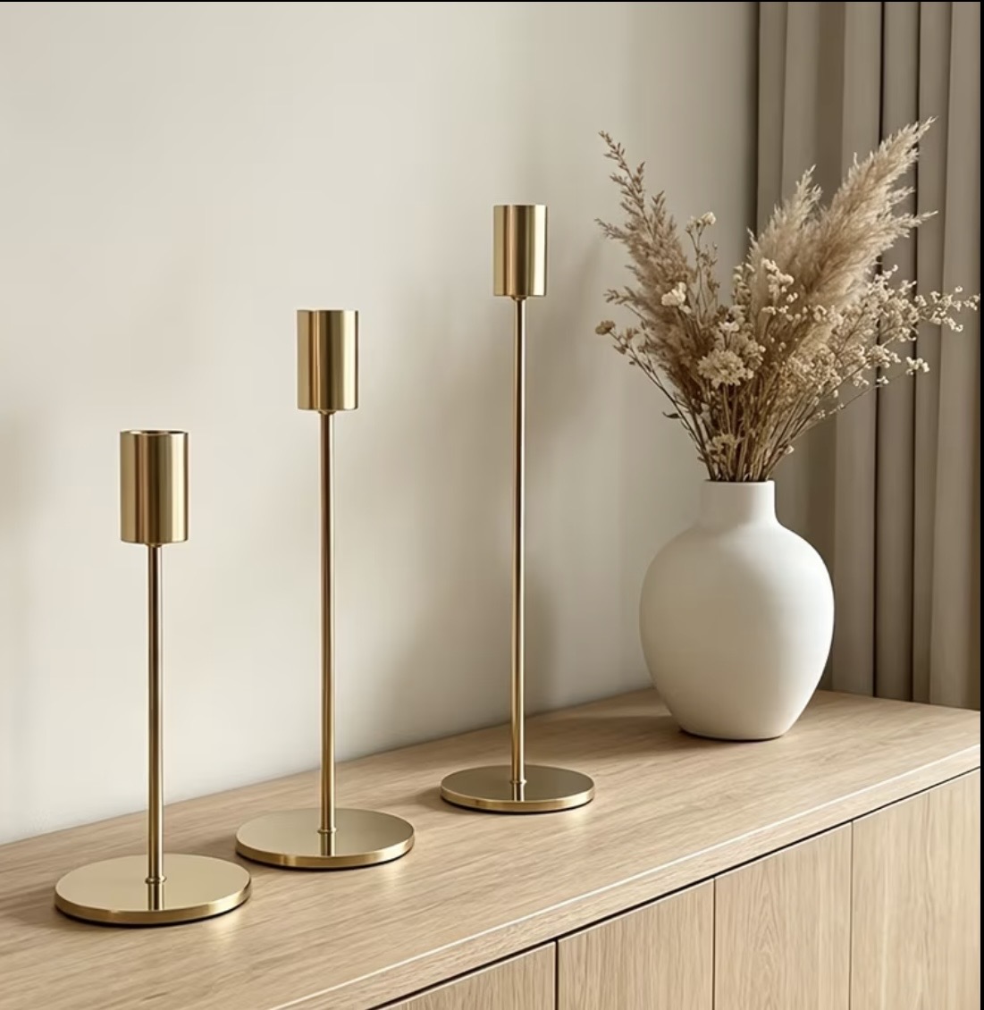 Minimalist gold tube-top candlesticks beside dried pampas grass
