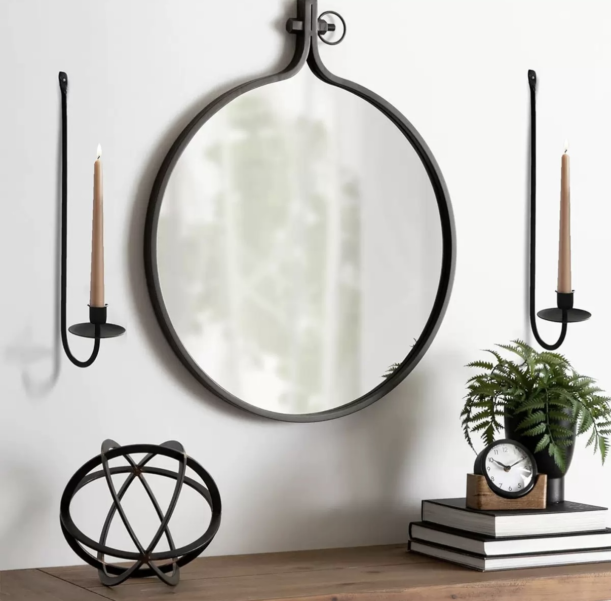 Pair of slim black wall-mounted taper candle holders beside a round mirror