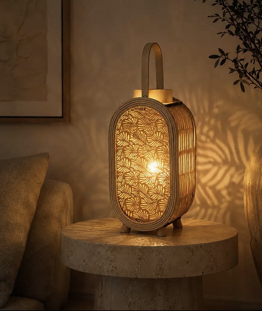 Woven rattan candle lantern glowing with warm leaf shadows