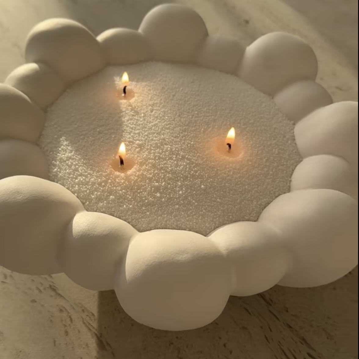 Ivory candle sand burning in a sculptural cloud-edge bowl