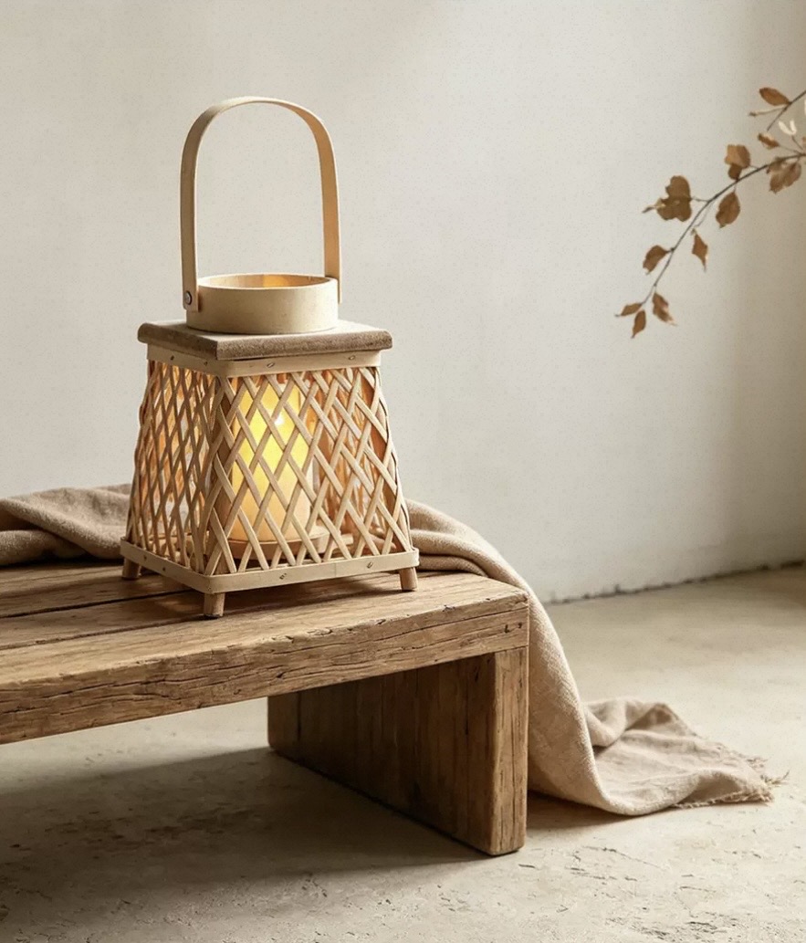 Woven bamboo candle lantern with handle glowing on a wooden bench