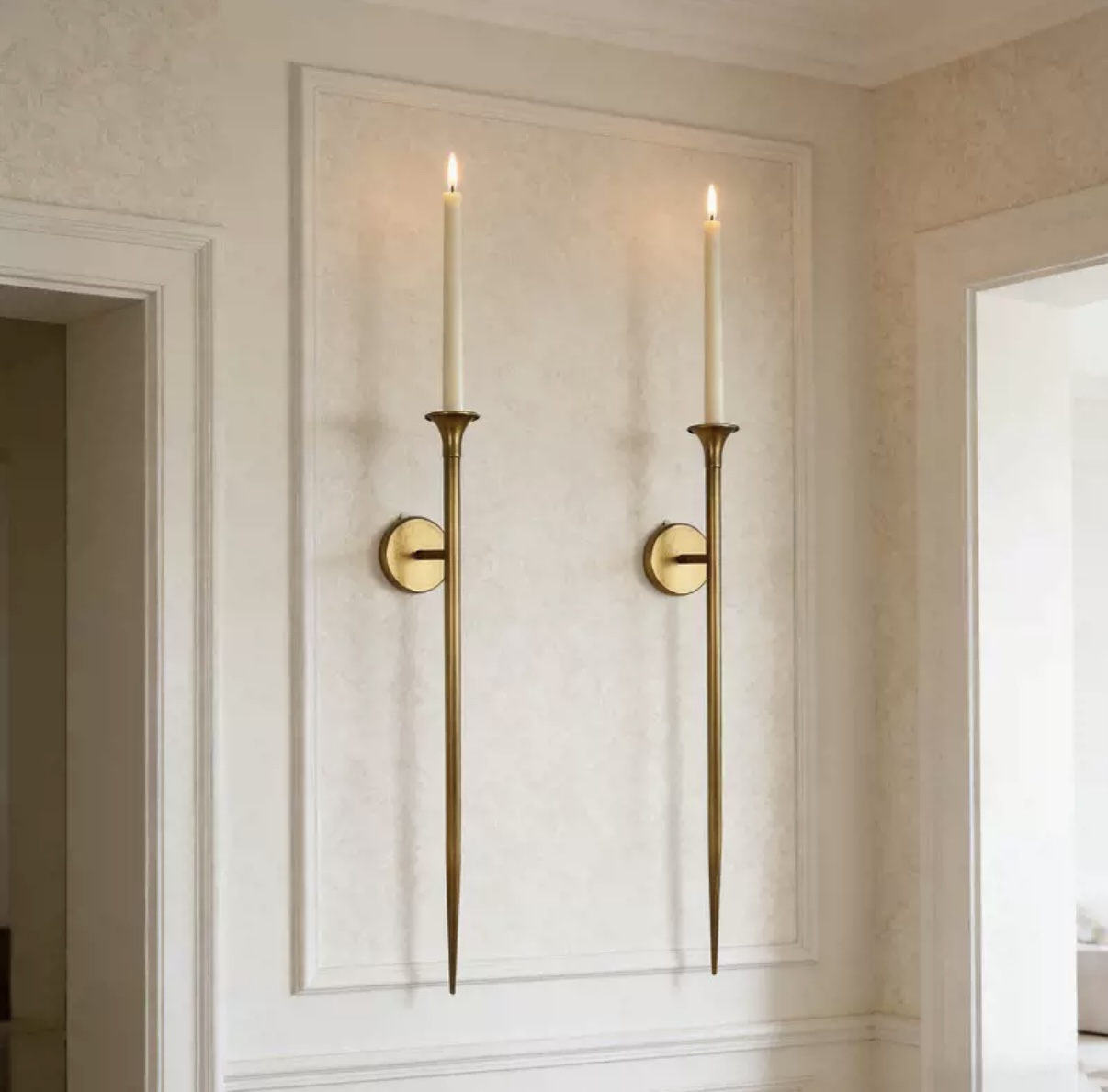 Pair of long brass wall-mounted taper candle holders in a bright interior