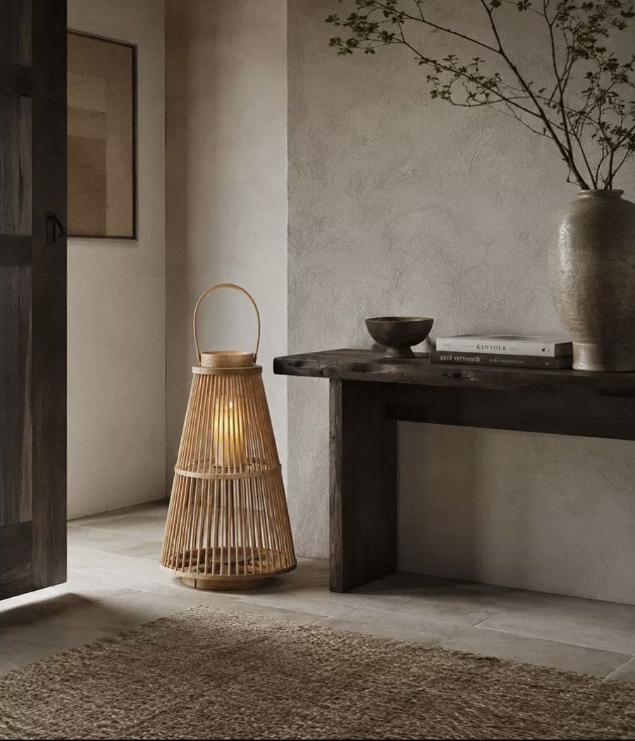 Tall slatted bamboo floor lantern glowing beside a console table